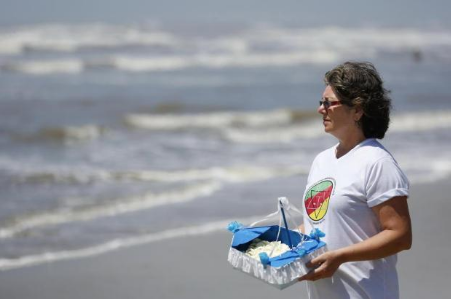 Maria Inês, diretora de projetos da FAUERS, entrega a sua oferenda à Iemanjá na praia do Rio Grande do Sul (Foto:Mateus Bruxel/Agencia RBS)